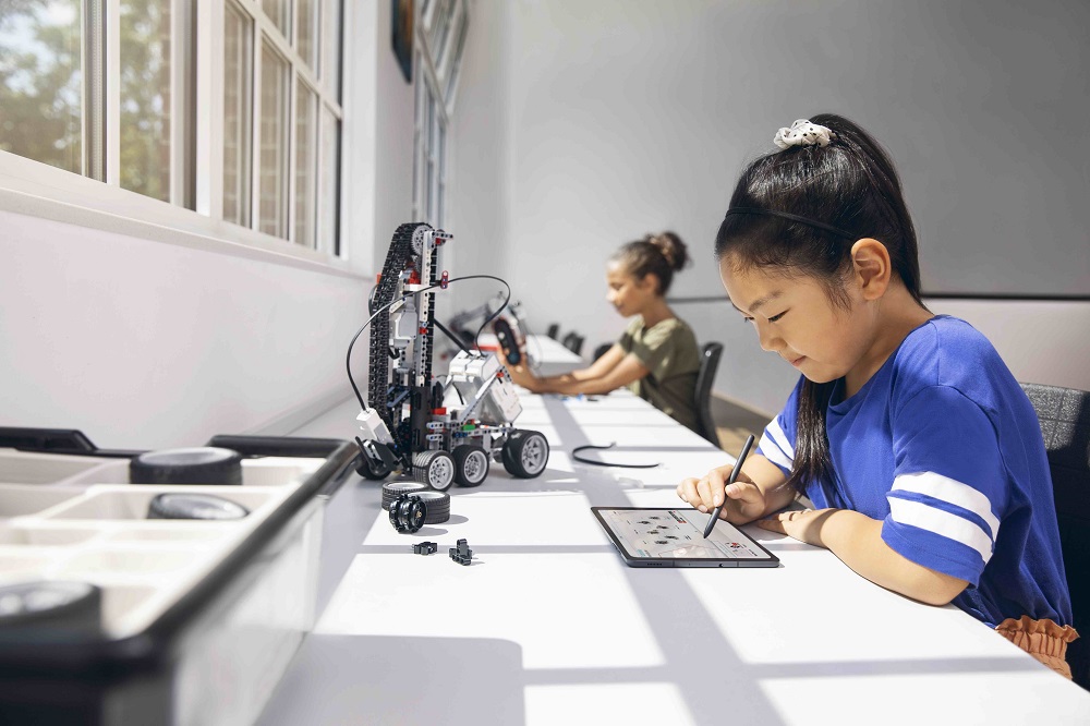 Samsung_Neues_Lernen_Technik_1000x666 Eine Frau steht vor einem Whiteboard und spricht vor zwei anderen Frauen, die an einem Tisch sitzen.