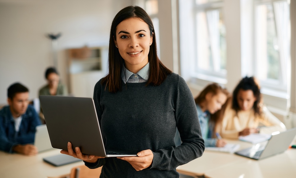 Smiling,Teacher,Using,Laptop,During,Computer,Class,At,High,School Converge Karriere