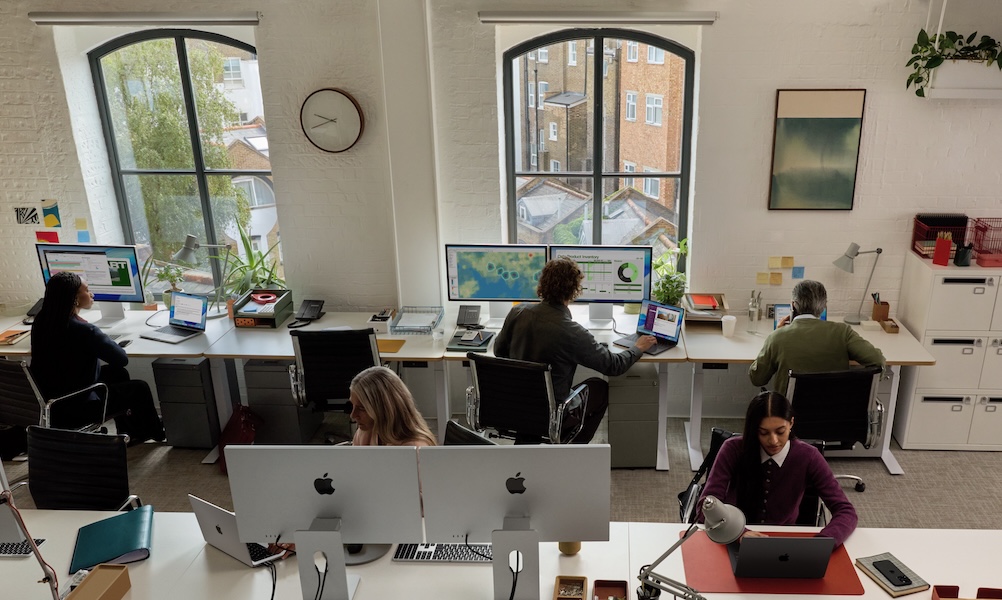 Eine Frau steht vor einem Whiteboard und spricht vor zwei anderen Frauen, die an einem Tisch sitzen.
