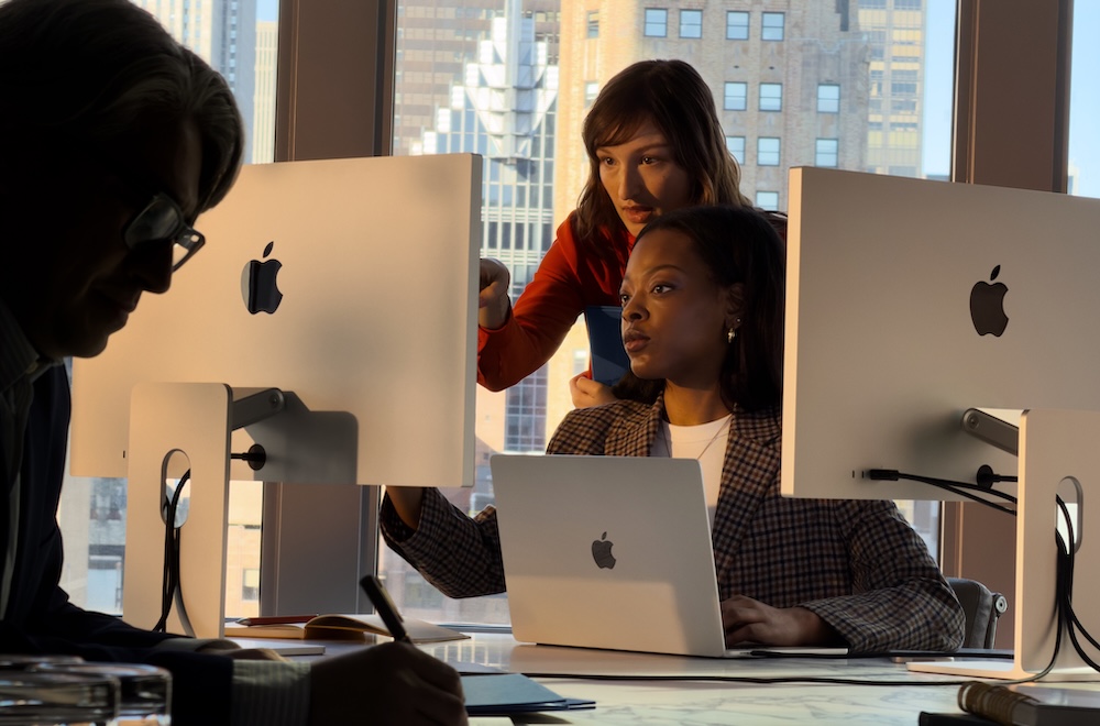Eine Frau und ein Mann sitzen an einem Tisch auf dem ein Laptop steht und schauen auf einen Notizblock.